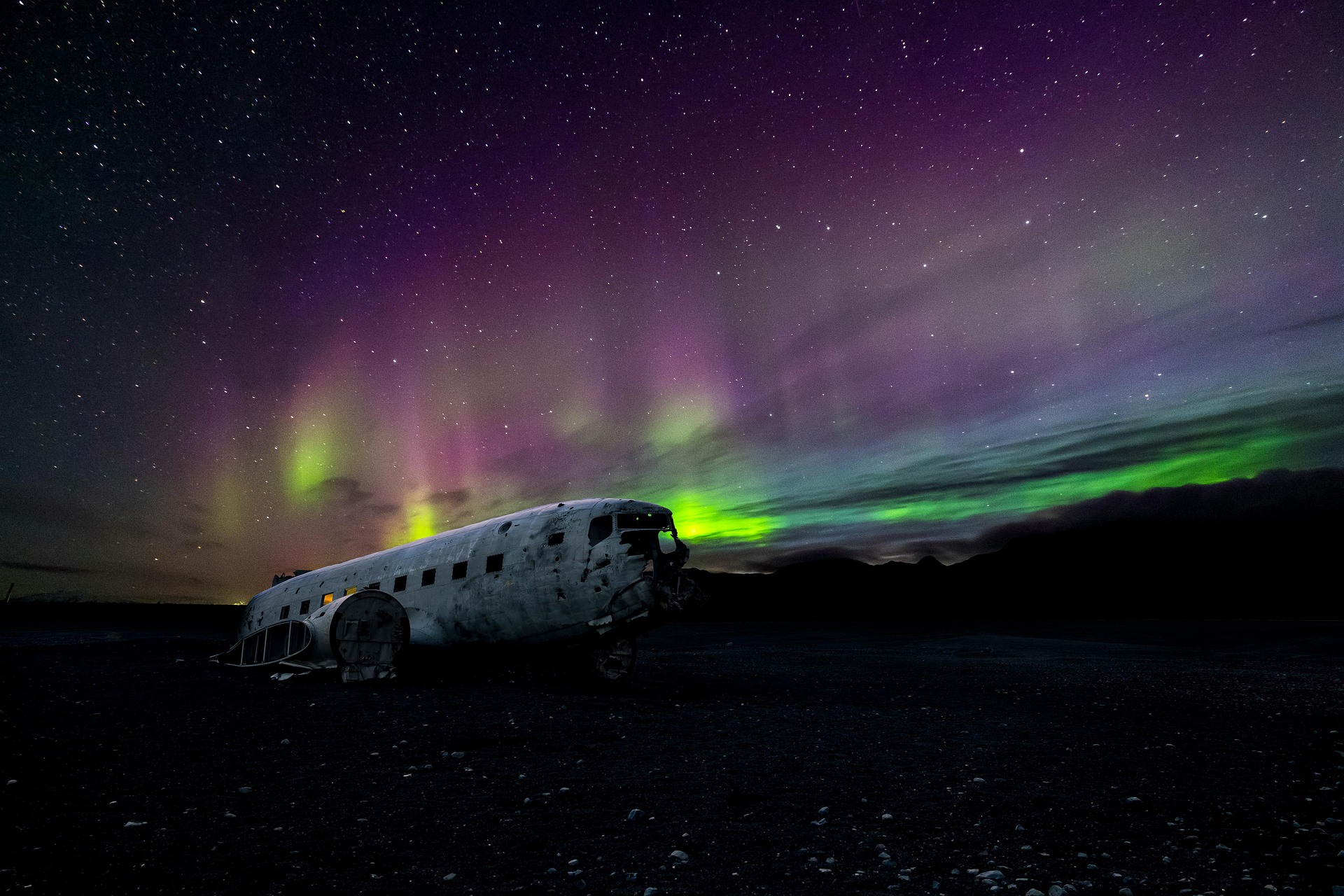 Rare purple and pink aurora borealis dominating the sky above abandoned DC-3 plane wreck in Iceland